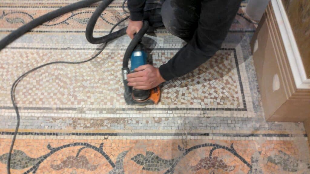 Skilled worker restoring an intricate mosaic floor with a handheld grinder.
